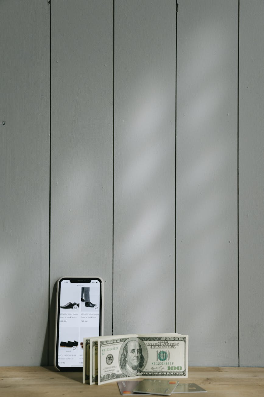 100 dolarlık banknot, ahşap masa, akıllı cihaz içeren Ücretsiz stok fotoğraf